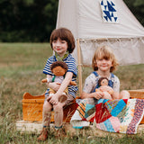 2 children sitting inside on a wooden boat with one holding a dinkum doll that's wearing the Olli Ella rambler dinkum doll outfit set available at Babipur. 