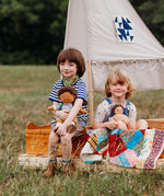 2 children sitting inside on a wooden boat with one holding a dinkum doll that's wearing the Olli Ella rambler dinkum doll outfit set available at Babipur. 