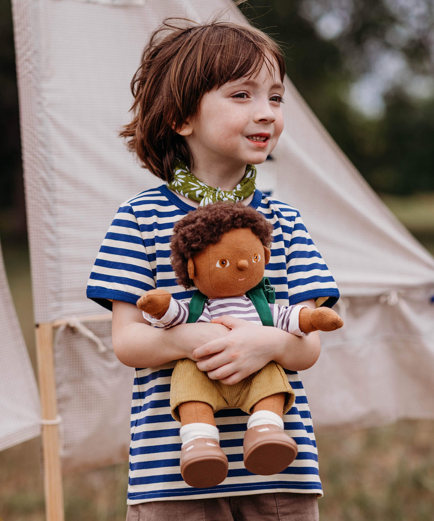 A child playing outside and holding a dinkum doll that's wearing the Olli Ella rambler dinkum doll outfit set available at Babipur. 