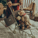 A child pushing two Olli Ella Cosy Dinkum Dolls in an Olli Ella Stroller. The child has the Garland Changing Bag hanging from their wrist, which can also be adjusted to fit over the shoulder.