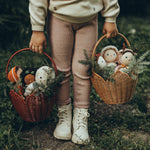 A child is holding a Natural and Red Olli Ella Rattan Poinsettia carry basket by the handles, each basket is filled with Christmas Jolly Dolly  Dinky Dinkum dolls, and the basket is decorated with pine tree branches