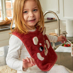 A child sat in a kitchen, wearing the Roommate Organic Cotton Baby Bib - Red Panda