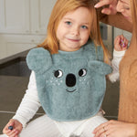 A child sat down with an adult, wearing the Roommate Organic Cotton Baby Bib - Koala