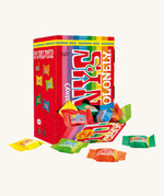 Tony's Chocolonely Fairtrade, Organic Tiny Tony's Rainbow Mix is a rainbow stripe box with 100 individually wrapped milk chocolate buttons in rainbow wrapping. The image shows the box open at the bottom, with individual wrapped chocolates scattered in front of the box. The image is on a cream background