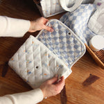 Avery Row Travel Changing Mat - Coastline in adults hands, un-poppered to show the blue and white checkerboard print inside on a wooden table.