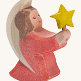 A Ostheimer wooden angel figure holding a star, available at Babipur. This handmade and hand painted festive figure has a rose pink dress and brown hair holding a yellow star