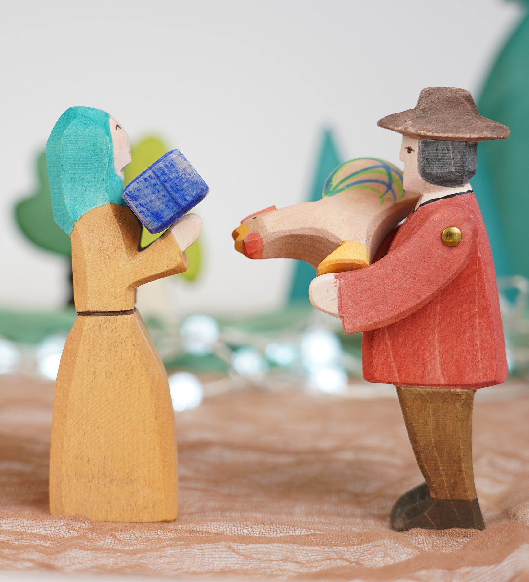 Ostheimer farmer man and Noah's wife wooden toy figures, handmade in Germany and exchanging a small gift and brown rooster in a waldorf and small world play scene, sold at Babipur