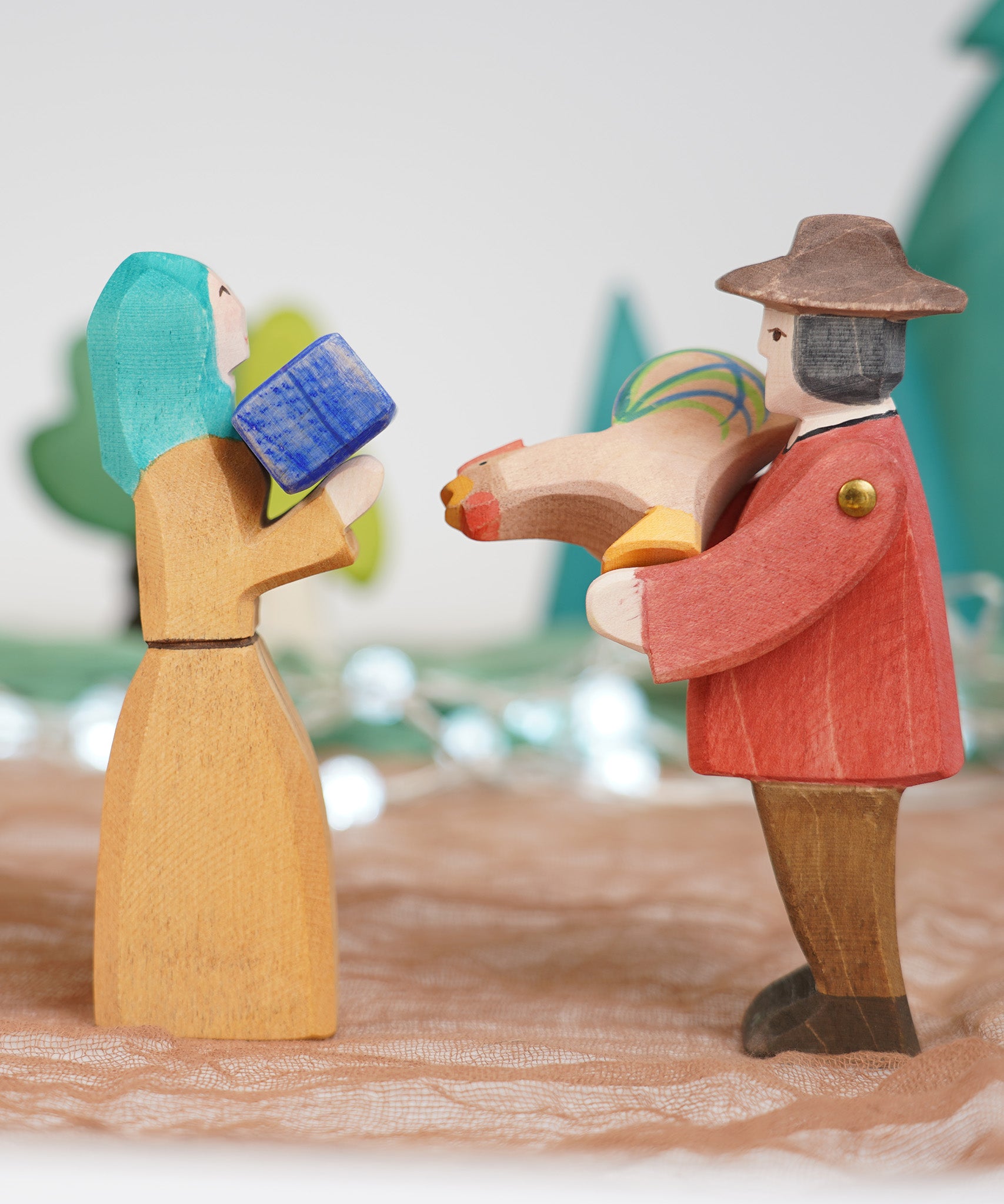 Ostheimer farmer man and Noah's wife wooden toy figures, handmade in Germany and exchanging a small gift and brown rooster in a waldorf and small world play scene, sold at Babipur