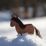 Ostheimer Hrokur Iceland Horse, wooden toy, brown with a dark brown mane and tail made from sisal and hemp fibres, stood in snow.