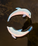 A close up of the Ostheimer wooden dolphin figure with its head held high and the diving dolphin floating on water and showing the hand painted detail.