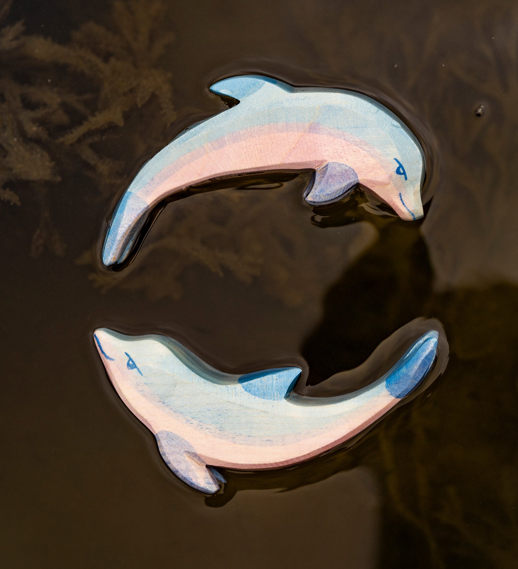 A close up of the Ostheimer wooden dolphin figure with its head held high and the diving dolphin floating on water and showing the hand painted detail.