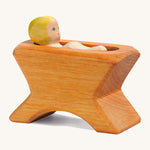 A Ostheimer wooden brown crib with a child lying inside the crib on a cream background.