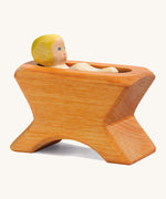 A Ostheimer wooden brown crib with a child lying inside the crib on a cream background.