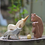 Ostheimer Bear with Cub, Howling Wolf, and Unicorn wooden figures gathered around a beehive, handmade in Germany, natural play scene on tree stump, Waldorf small world toy, sold at Babipur