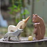 Ostheimer Bear with Cub, Howling Wolf, and Unicorn wooden figures gathered around a beehive, handmade in Germany, natural play scene on tree stump, Waldorf small world toy, sold at Babipur