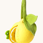 The Lou the Lemon Pacifier Holder on a cream background. The image shows an Oli & Carol lemon teething toy half way inside the holder. The lemon is textured and has a green muslin leaf attachment on the top to tie the holder to a pram handle, high chair etc.