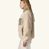 side view of woman wearing Patagonia Women's Classic Retro-X® Fleece Jacket in Dark Natural w/River Rock Green, green zip pocket visible. 