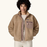 Woman wearing Patagonia Women's Classic Retro-X® Fleece Jacket in oar tan, undone zip, hands in both side pockets. 