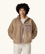 Woman wearing Patagonia Women's Classic Retro-X® Fleece Jacket in oar tan, undone zip, hands in both side pockets. 
