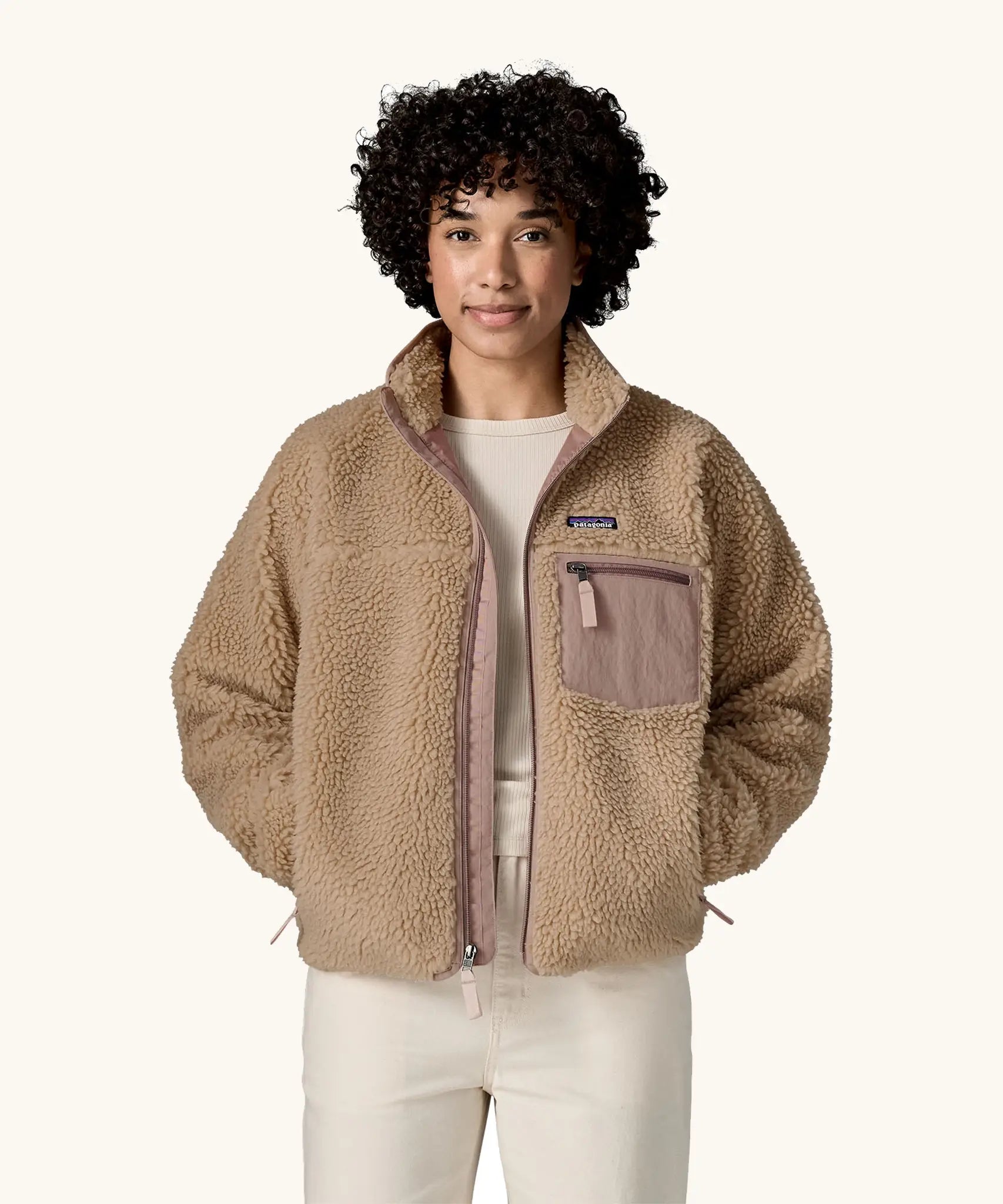 Woman wearing Patagonia Women's Classic Retro-X® Fleece Jacket in oar tan, undone zip, hands in both side pockets. 