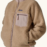 Woman wearing Patagonia Women's Classic Retro-X® Fleece Jacket in oar tan, fully zipped, hands in pockets, closer view of chest pocket. 