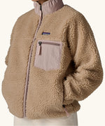Woman wearing Patagonia Women's Classic Retro-X® Fleece Jacket in oar tan, fully zipped, hands in pockets, closer view of chest pocket. 