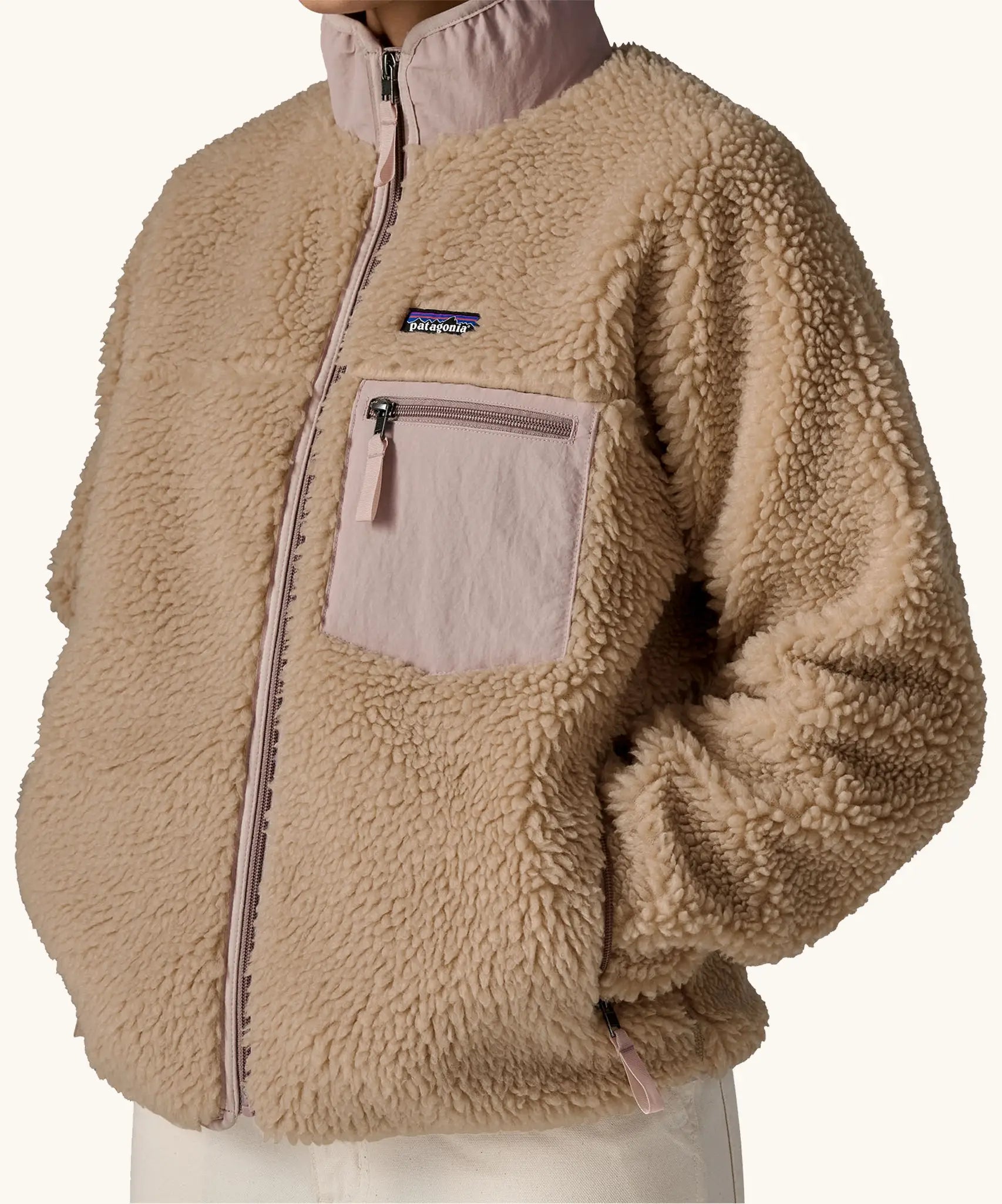 Woman wearing Patagonia Women's Classic Retro-X® Fleece Jacket in oar tan, fully zipped, hands in pockets, closer view of chest pocket. 