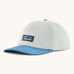 Patagonia p6 label trad cap in white with a blue visor. Shows air holes on the top and brand patch on the front