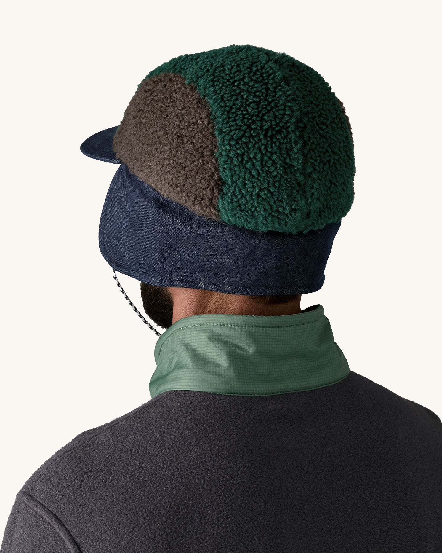 Back of man wearing Patagonia Adult Range Earflap Cap in denim, and cascade fleece with denim flap down and tied at the chin, for sale at Babipur.
