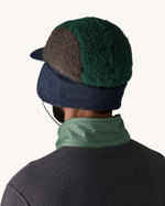 Back of man wearing Patagonia Adult Range Earflap Cap in denim, and cascade fleece with denim flap down and tied at the chin, for sale at Babipur.
