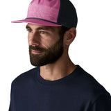 Man wearing Patagonia's airfarer cap in pink with blue mesh back panel.  Hat has a trucker style and wide brim