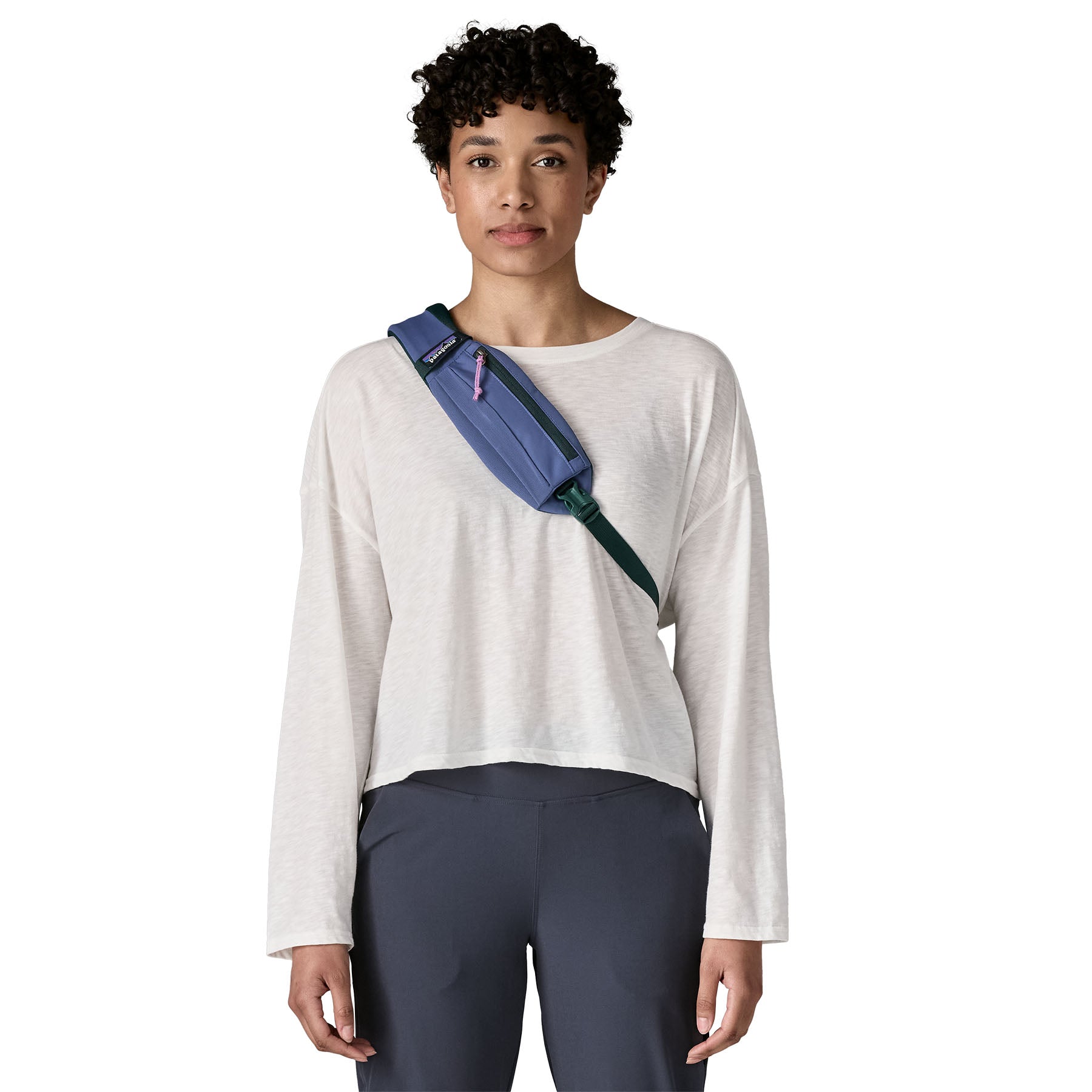 A woman wearing the Patagonia atom 8 litre sling bag in current blue available at Babipur showing the small zipped pocket on the shoulder strap