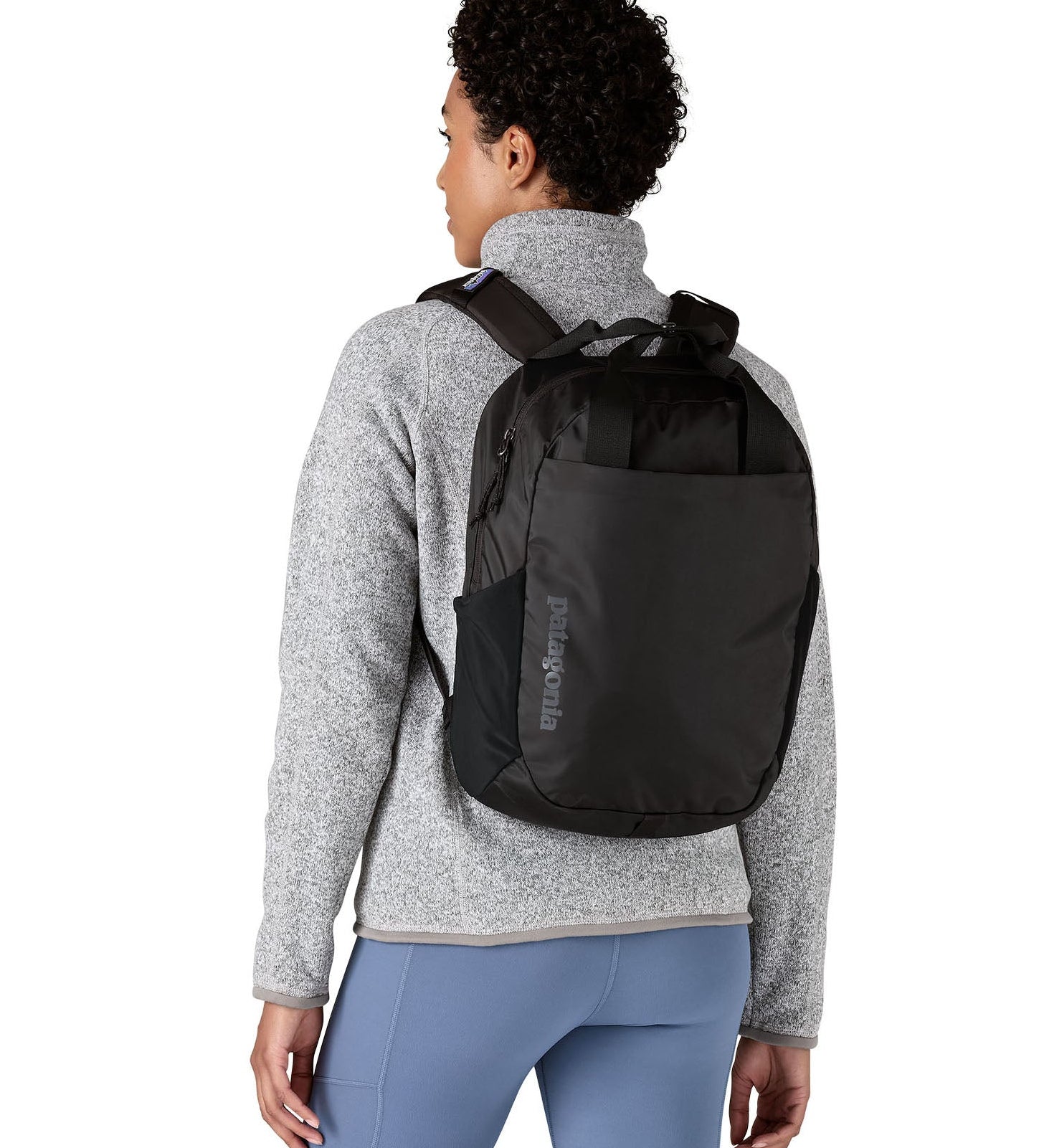 Woman wearing Patagonia's atom 20 litre tote pack in black with matching  handle zipped compartment and side pocket