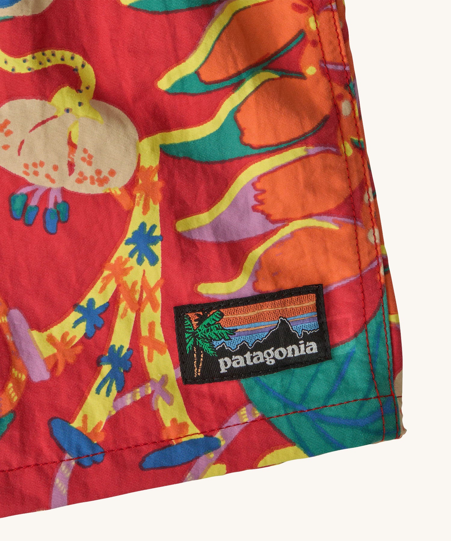 Close up of Patagonia baby baggies quick drying shorts in red with repeating abstract floral design. Shows brand patch on the hem