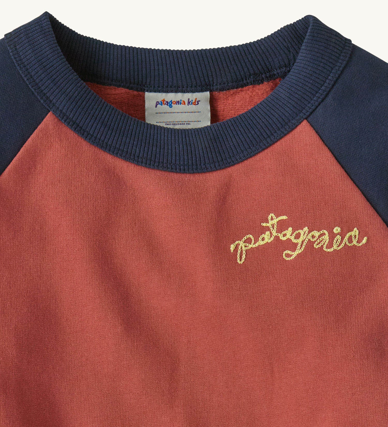 A close up of the Patagonia Baby Crew Sweatshirt in wiggle fitz / potters red showing the navy collar and brand name stitch detail