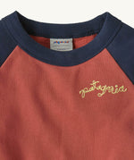 A close up of the Patagonia Baby Crew Sweatshirt in wiggle fitz / potters red showing the navy collar and brand name stitch detail