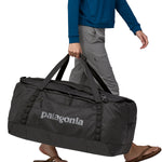 A person carrying the Patagonia Black Hole Duffel 100L Black with the carry handles
