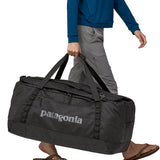 A person carrying the Patagonia Black Hole Duffel 100L Black with the carry handles