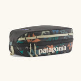 Patagonia black hole cube 3 litre bag in black with repeating abstract print design on top panel. Shows cream zip detail and great straps
