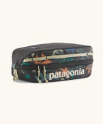 Patagonia black hole cube 3 litre bag in black with repeating abstract print design on top panel. Shows cream zip detail and great straps