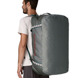 A man carrying the Patagonia black hole 100L duffel bag in noble grey on his back by the shoulder straps. Backpack available at Babipur. 