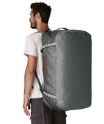 A man carrying the Patagonia black hole 100L duffel bag in noble grey on his back by the shoulder straps. Backpack available at Babipur. 