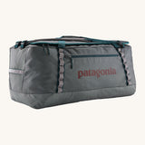 Patagonia black hole 100L duffel bag in noble grey available at Babipur. A dark grey bag with green trim and brown branding on the side. Features shoulders straps and a handle on the top for easy carrying.