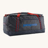 Patagonia black hole 100L duffel bag in smolder blue / amanita red available at Babipur. A dark blue bag with red trim and blue branding on the side. Features shoulders straps and a handle on the top for easy carrying.