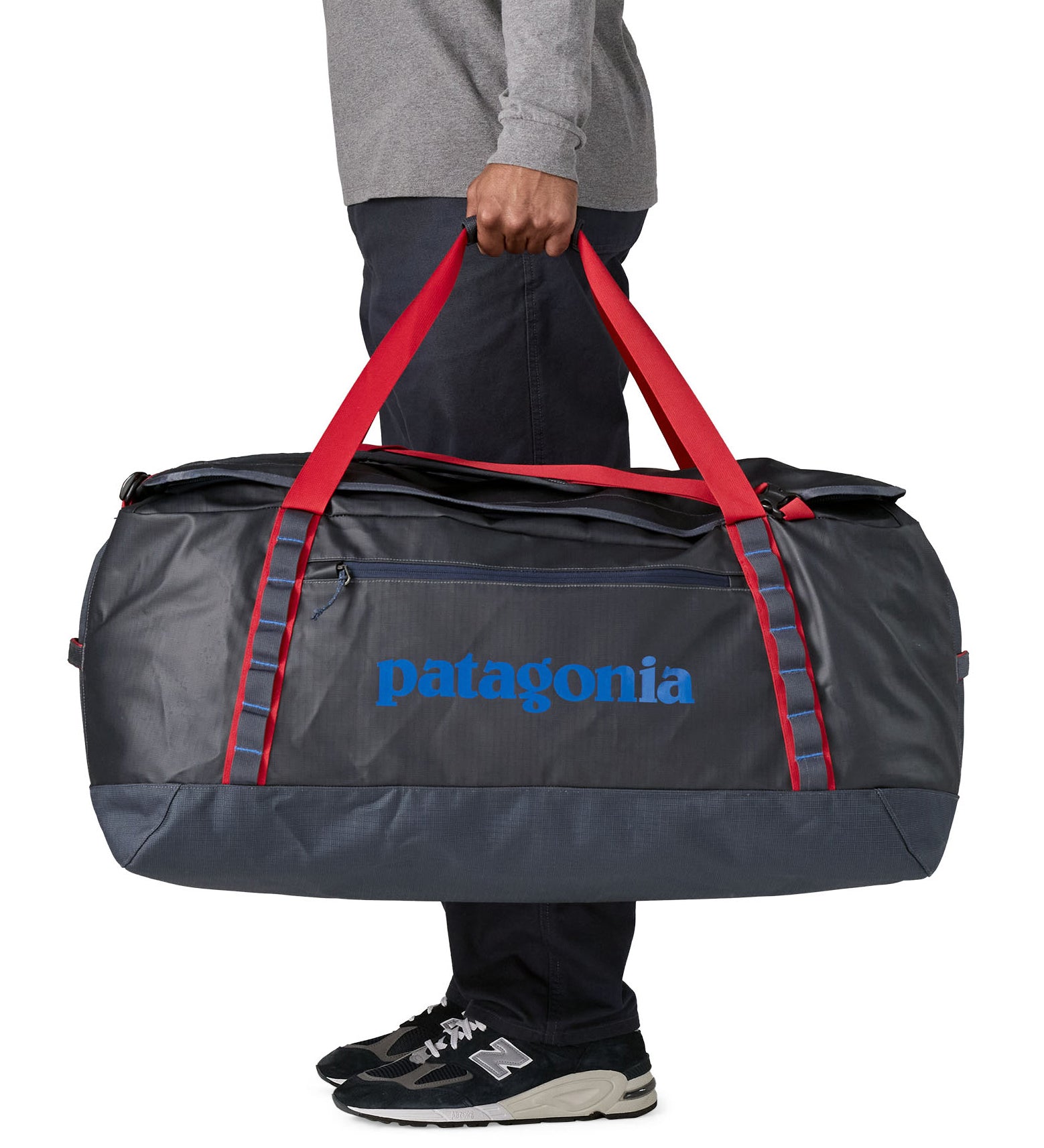 A man carrying the Patagonia black hole 100L duffel bag in smolder blue / amanita red available at Babipur. 