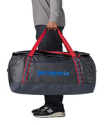 A man carrying the Patagonia black hole 100L duffel bag in smolder blue / amanita red available at Babipur. 