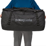 A person holding the Patagonia Black Hole Duffel 100L Black in their hands to show the size