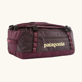 Patagonia black hole 70L duffel bag in Berry Fig. A deep maroon bag with yellow trim and Patagonia branding on the side. Features shoulders straps and a handle on the top for easy carrying.