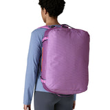 A woman carrying the Patagonia black hole 40l duffel bag in brisk purple on her back by the shoulder straps. Backpack available at Babipur. 