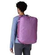 A woman carrying the Patagonia black hole 40l duffel bag in brisk purple on her back by the shoulder straps. Backpack available at Babipur. 